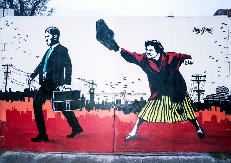 May include: A street art mural depicting two figures, one in a suit carrying a briefcase and the other throwing a shoe. The background features a cityscape with power lines and birds in flight. The text "Hop Jonie" is visible in the upper right corner.