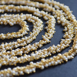 Puede incluir: Un collar de cadena dorada con pequeñas cuentas blancas. La cadena está en capas y retorcida, creando un diseño único e intrincado.