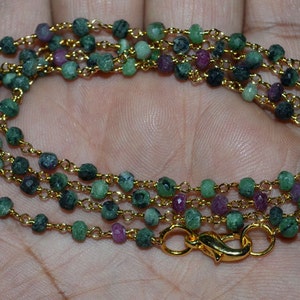 Puede incluir: Un collar con pequeñas cuentas facetadas en tonos verdes y rojos, ensartadas en una delicada cadena dorada. El collar tiene un cierre dorado. Las cuentas miden aproximadamente 3 mm de diámetro.