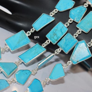 May include: A silver chain necklace with turquoise gemstone links. The turquoise stones are cut into various shapes, including rectangles and irregular shapes. The chain is made of silver and has a polished finish.
