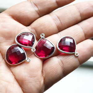 Könnte beinhalten: Vier facettierte, tropfenförmige Anhänger aus rotem Edelstein mit silbernen Ösen.