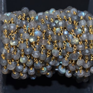 May include: A strand of gray labradorite gemstone beads with gold chain links. The beads are faceted and have a shimmery, iridescent quality.