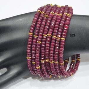May include: A stack of 10 red ruby gemstone bracelets with gold beads. The bracelets are on a black mannequin arm.