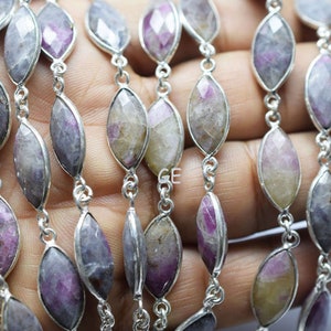 May include: A strand of faceted, marquise-shaped gemstone beads with a silver chain. The beads are a mix of purple, pink, and white with a slight yellow hue.