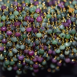 Può includere: Primo piano di una catena d'oro con perline di pietre preziose verdi e rosa. La catena è avvolta attorno a una bobina.