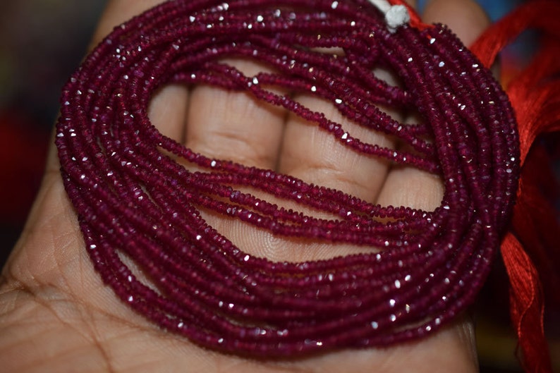 May include: A strand of deep red ruby beads, faceted and strung together. The beads are small and uniform in size, creating a smooth and elegant look.