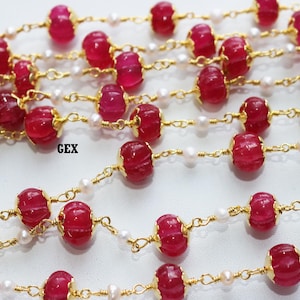 May include: A gold chain necklace with red and white beads. The red beads are carved with a pattern and have a gold trim. The white beads are small and round.