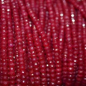 May include: A strand of deep red faceted gemstone beads. The beads are small and round, and they are strung together on a clear thread.