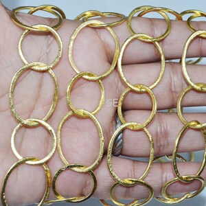 May include: Gold chain made of linked oval rings. The chain is textured and has a shiny finish.