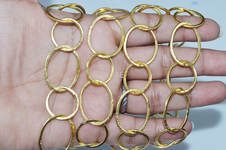 May include: Gold chain made of linked oval rings. The chain is textured and has a shiny finish.