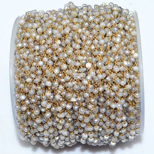 May include: A silver and gold chain made of small, faceted beads. The chain is wound around a spool.