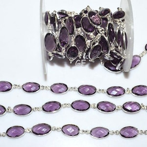 May include: A silver chain with oval-shaped amethyst gemstones. The chain is coiled on a spool and laid out straight to show the design.
