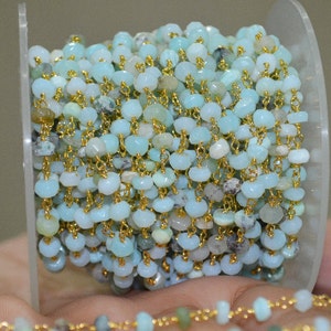 May include: A spool of light blue opal beads strung on a gold chain. The beads are faceted and have a slightly iridescent sheen.