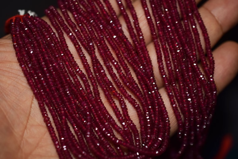 May include: Strands of faceted, deep red beads. The beads are small and uniform in size, creating a rich, textured appearance. The beads are likely strung together to create a necklace or bracelet. The color is a vibrant, saturated red.