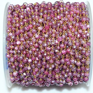 Op de afbeelding: Een spoel met roze robijn edelsteen kralen geregen aan een gouden ketting. De kralen zijn gefacetteerd en hebben een licht onregelmatige vorm. De ketting is delicaat en heeft een fijne maat.
