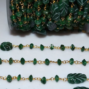 May include: A strand of green gemstone beads with gold chain links. The beads are faceted and some are carved into leaf shapes.