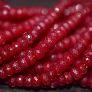 May include: A close-up of a strand of red gemstone beads. The beads are faceted and have a shiny, polished finish.