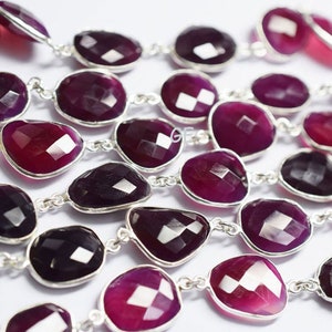 Könnte beinhalten: Eine Strähne aus facettierten violetten Edelsteinperlen mit silbernen Verbindungselementen. Die Perlen sind oval geformt und haben eine glatte, polierte Oberfläche.
