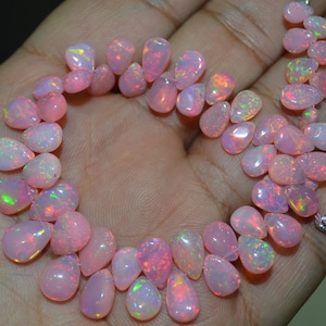 May include: A strand of pink opal gemstone beads in a teardrop shape. The beads are strung on a clear thread and are arranged in a circle.