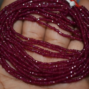 May include: A strand of deep red ruby beads, faceted and strung together. The beads are small and uniform in size, creating a smooth and elegant look.