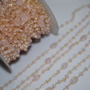 May include: A spool of gold chain with pink rose quartz beads. The chain is strung with small, round beads and larger, oval-shaped beads. The chain is laid out in a straight line, showing the pattern of the beads.