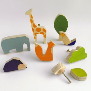 Könnte beinhalten: Ein Set aus neun Holz-Knöpfen mit Tier- und Naturmotiven. Die Knöpfe zeigen Giraffe, Elefant, Fuchs, Baum, Wolke und Blatt. Die Knöpfe sind in verschiedenen Farben bemalt, darunter Orange, Blau, Grün und Lila.