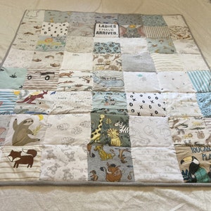 May include: A patchwork quilt made from baby clothes with a variety of animal prints and designs. The quilt is made up of squares of different fabrics, each with a different design. The quilt is a light blue and white color scheme. The quilt has a gray border and is made of soft, comfortable fabric.
