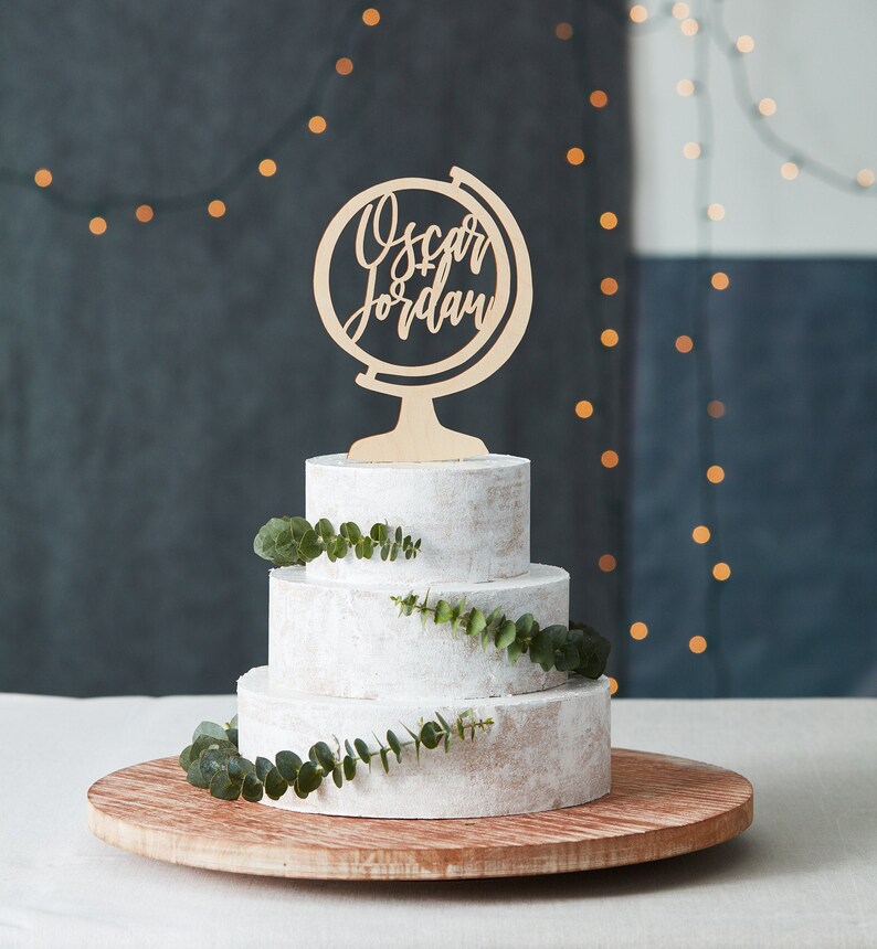 K&ouml;nnte beinhalten: Eine dreist&ouml;ckige wei&szlig;e Torte, verziert mit Gr&uuml;n und gekr&ouml;nt mit einem Holz-Globus-Tortenaufsatz mit der Aufschrift "Oscar Jordan".