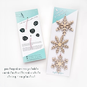 May include: Set of three wooden snowflake ornaments with red and white string. The ornaments are packaged on recyclable cardstock with the text "wooden ornaments!" and "light & paper".