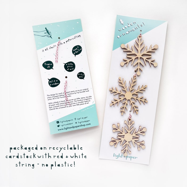 May include: Set of three wooden snowflake ornaments with red and white string. The ornaments are packaged on recyclable cardstock with the text "wooden ornaments!" and "light & paper".