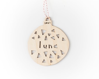 May include: A wooden Christmas ornament shaped like a bauble with the name "Luna" cut out and the year "2021" engraved on the top. The ornament is decorated with a pattern of small triangles.