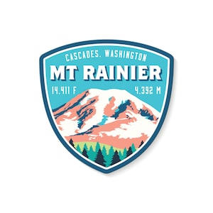 May include: A blue and white sticker with a mountain range illustration and the text "MT RAINIER" in white. The sticker also includes the text "CASCADES, WASHINGTON" and the mountain's height in feet and meters: "14,411 F" and "4,392 M".