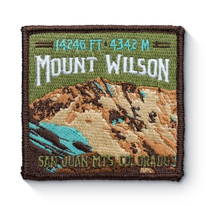 Könnte beinhalten: Ein brauner gestickter Aufnäher mit grünem Hintergrund. Der Aufnäher zeigt eine Bergkette mit einem türkisfarbenen See und dem Text "14246 FT 4342 M MOUNT WILSON SAN JUAN MTS COLORADO".