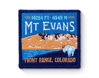 Puede incluir: Parche bordado azul y blanco con el texto "MT EVANS" y "FRONT RANGE, COLORADO". El parche también presenta una cordillera y una cabra montés blanca.
