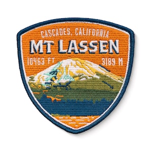 Puede incluir: Un parche bordado de color naranja, azul y verde con el texto "CASCADES, CALIFORNIA MT LASSEN 10463 FT 3189 M" y una representación de una montaña.