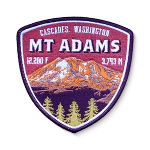 May include: A purple and red embroidered patch with the text "CASCADES WASHINGTON MT ADAMS 12,280 FT 3,743 M" and an image of a mountain with snow on top. There are green trees at the bottom of the patch.