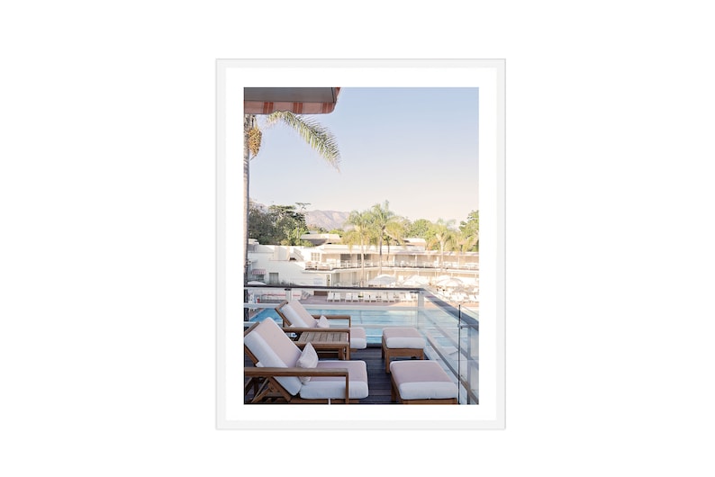 May include: A view from a balcony overlooking a swimming pool with lounge chairs and a palm tree in the foreground. The pool is surrounded by white buildings and lush greenery.