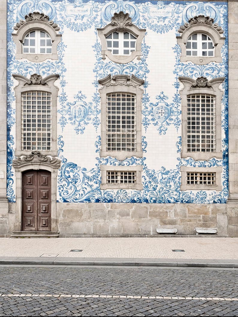 May include: A building facade with a white background and blue and white tile designs. The building has three windows with ornate frames and a wooden door. The tile designs feature floral patterns and the text "Ave Maria" and "Quinta Pena".