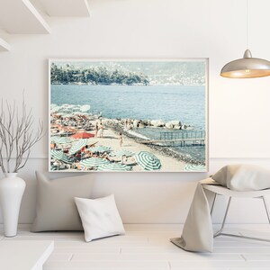 May include: A framed photograph of a beach scene with people relaxing under striped umbrellas. The beach is sandy with a clear blue ocean in the background. There are trees and buildings in the distance.