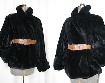 May include: A black faux fur jacket with a brown leather belt. The jacket has a shawl collar and long sleeves.