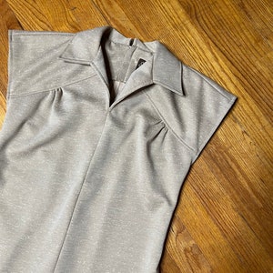 May include: A beige sleeveless dress with a collared neckline and a zipper closure in the back. The dress has a textured fabric with a subtle sparkle.