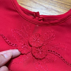 May include: Red dress with a floral embroidered neckline.
