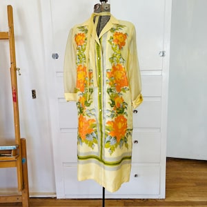 May include: A vintage yellow dress with long sleeves and a floral pattern of orange and green flowers. The dress is displayed on a mannequin and has a collared neckline and a button-down front. The dress is knee-length.