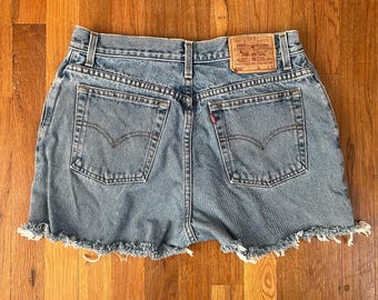 Puede incluir: Un par de pantalones cortos de mezclilla azul claro con bordes deshilachados. Los pantalones cortos tienen un parche de cuero marrón en la parte posterior con el texto "Levi Strauss & Co. Original  Quality Clothing" y "550".