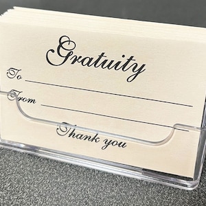 May include: A stack of white gratuity cards with black text, "Gratuity", "To", "From", and "Thank you", in a clear plastic holder.