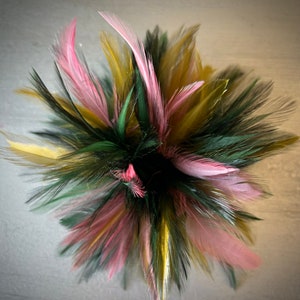 May include: A cluster of pink, green, and gold feathers arranged in a circular shape. The feathers are soft and fluffy, and they create a beautiful and delicate display.