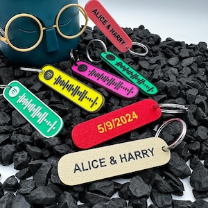 May include: A set of six keychains with different designs. The keychains are made of colourful plastic and feature a variety of designs, including a music note, a date, and the names "Alice & Harry".