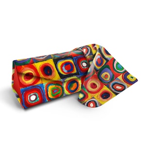 May include: A colorful eyeglass case with a geometric pattern of red, yellow, blue, and green circles and squares. The case is folded in half and the pattern is visible on both sides.