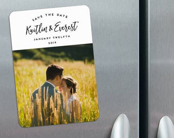 May include: Save the date magnet with a photo of a couple kissing in a field. The text reads "Save the Date Kaitlin & Everest January Twelfth 2019".