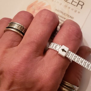 May include: White plastic ring sizer with black numbers and a white arrow. The sizer is marked with sizes 5 through 17. The text "PAT. PEND. 9101693" is printed on the sizer.